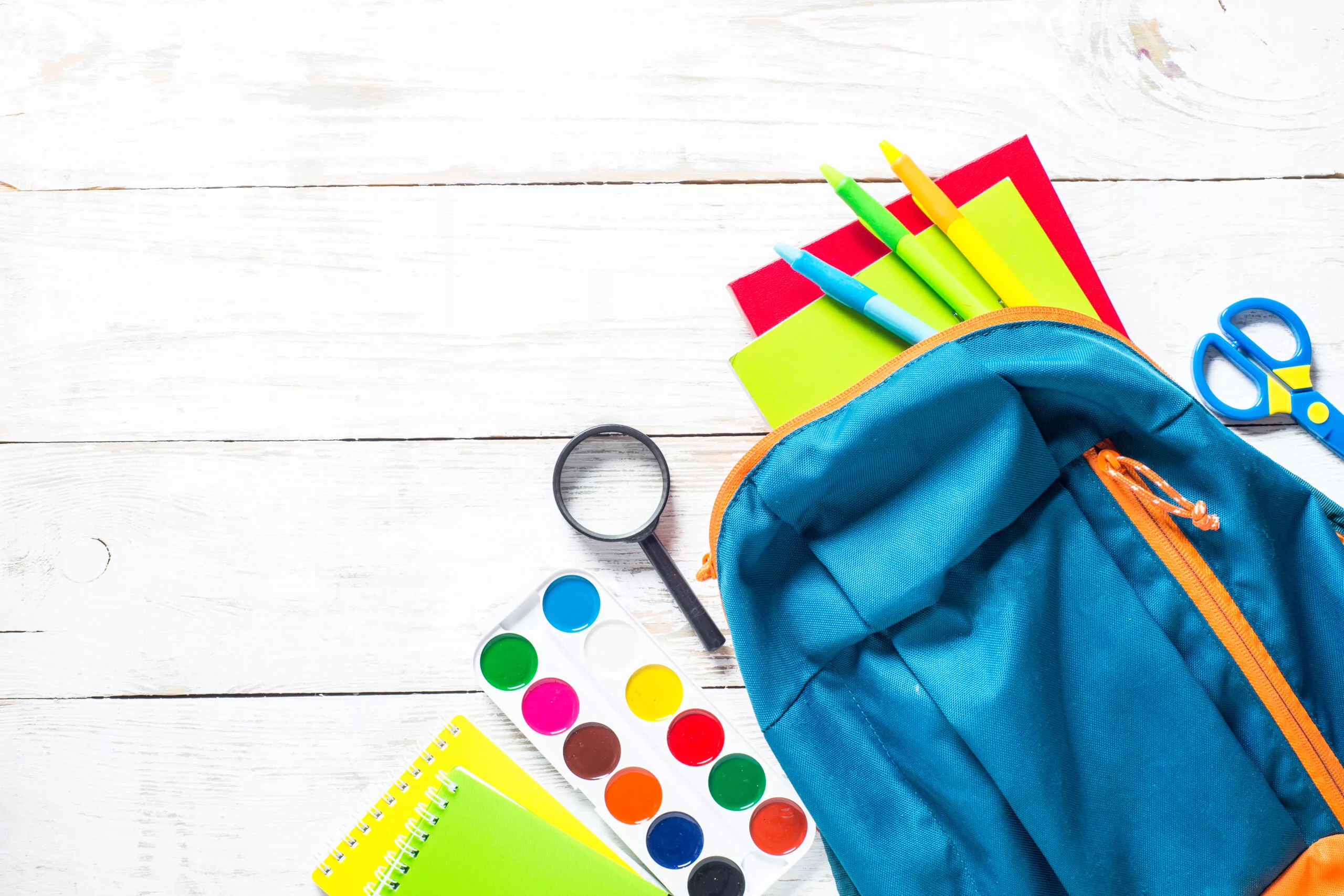 School education background. School backpack with stationery on white wooden table. Top view with copy space.